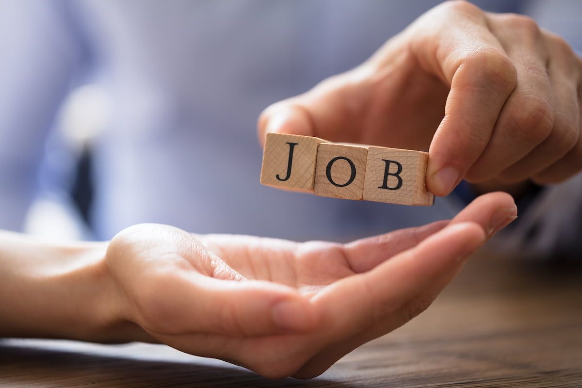 Mann in hellblauem Hemd mit drei Holzwürfeln in der Hand, die das Wort Job ergeben.